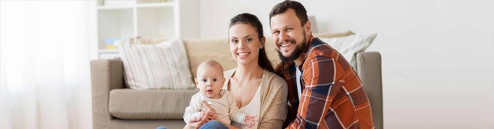 Husband, wife, and child sitting on the floor in front of their couch.